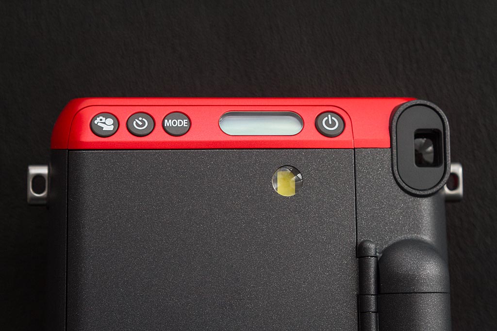 Le dos de l'Instax Mini 70 regroupe les accès à tous les contrôles. De gauche à droite : fonction Selfie, Retardateur, Mode de prise de vue, et interrupteur on/off placé de l'autre côté de l'écran digital.